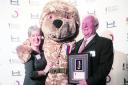 Rotary Club past president Colin Sweet and the H4H Bear hold the medal, while Bernice Brady, the club’s H4H co-ordinator, lends a hand